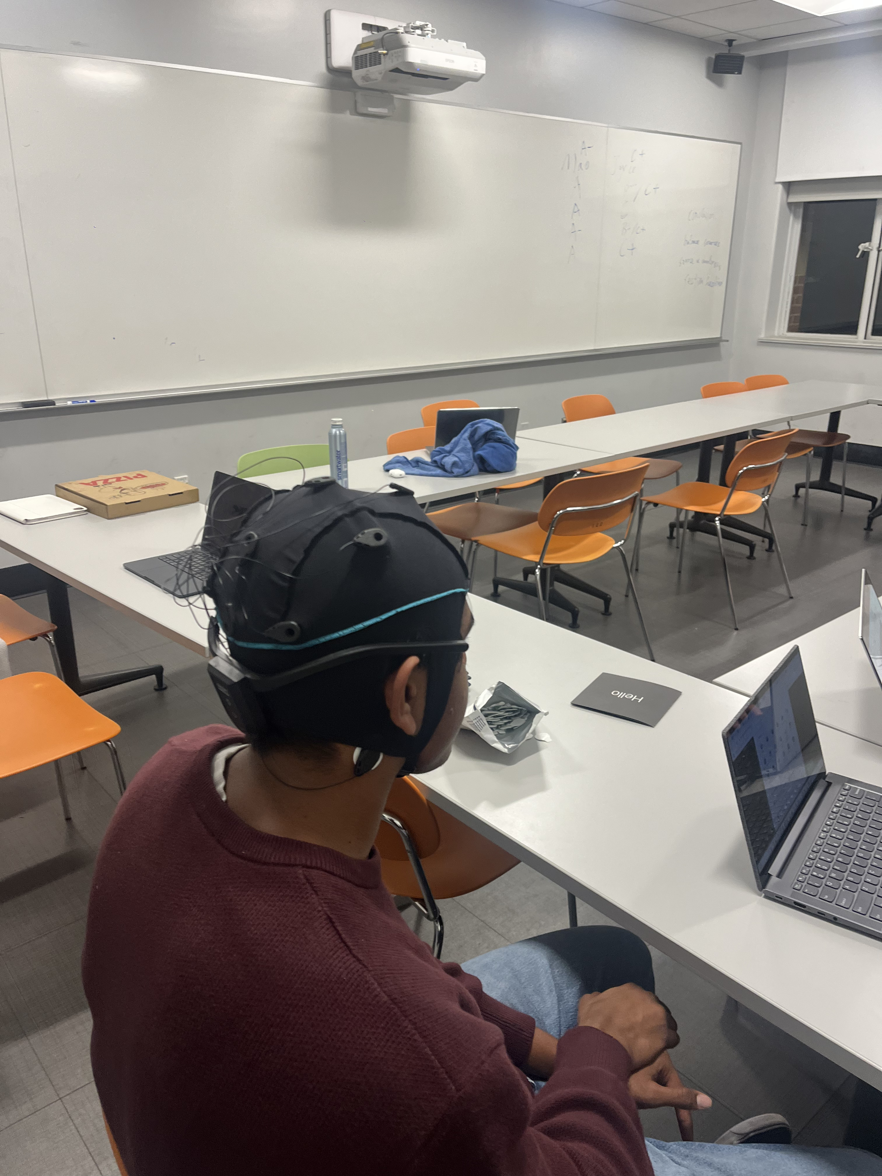 Person wearing discrete EEG cap while working at laptop in classroom setting